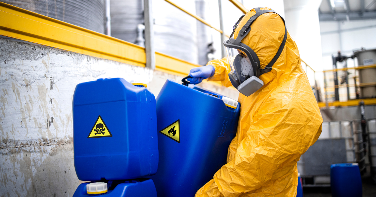 person in a hazmat suit handling drums of hazardous material